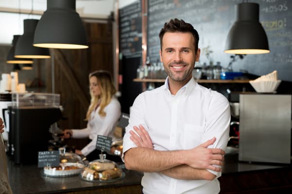 A young man stands in the coffee shop that owns, proudly smiling at the camera