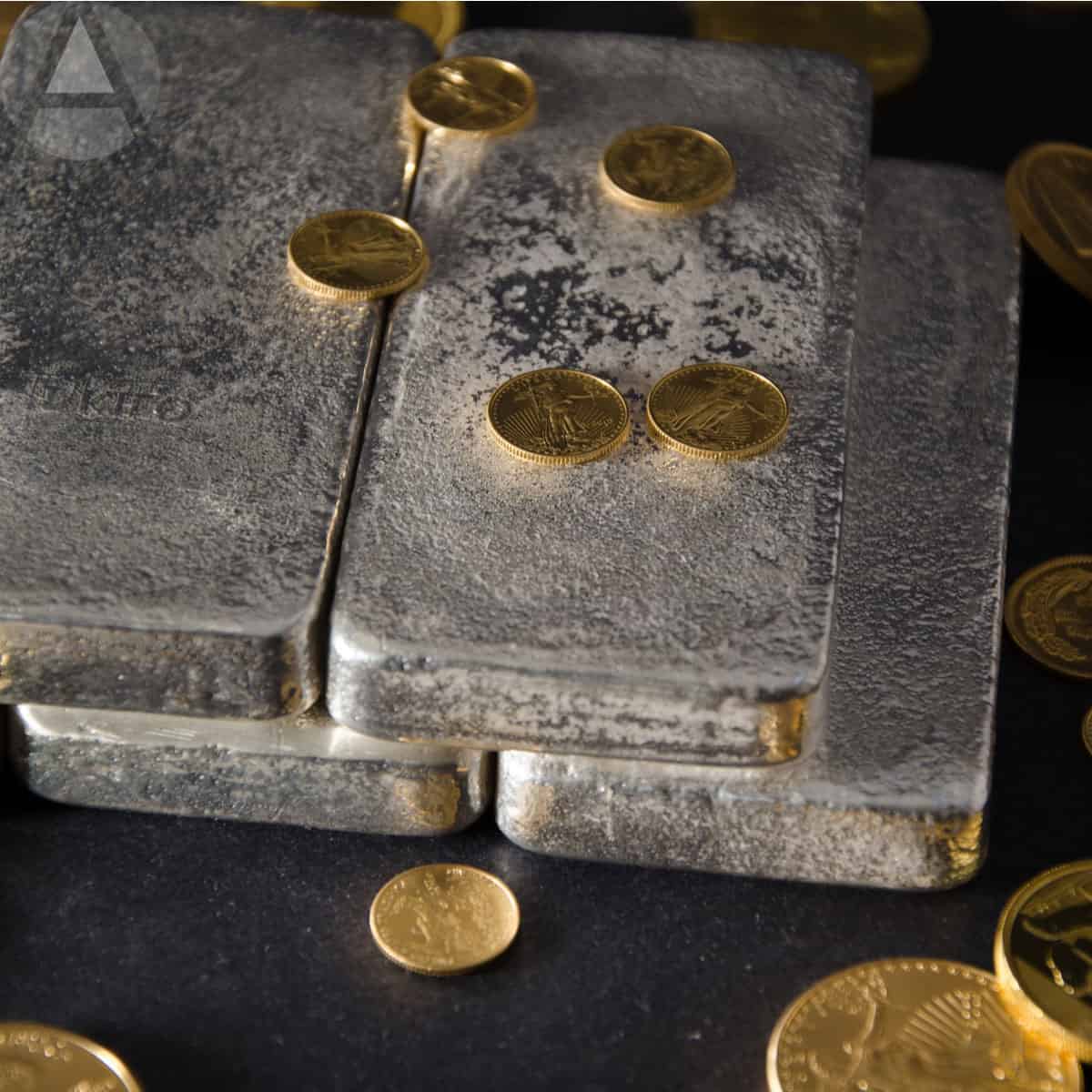 Silver bars and gold coins on a black surface representing assets for a precious metal IRA.